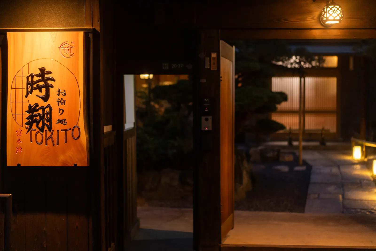 灯りの入った「時翔 お泊り処 TOKITO」の木の看板と、開かれた門口
