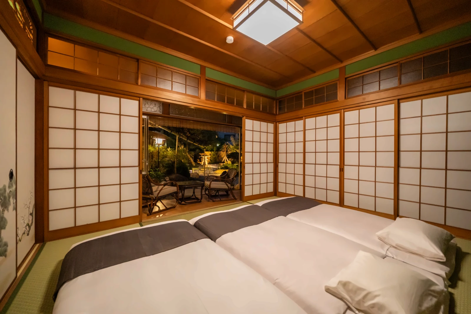 夜の畳の間に敷かれた床。開け放した障子の向こうに灯りのともる庭が見える